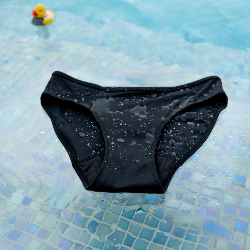 Black Sahara period swim brief with water droplets on a pool floor background