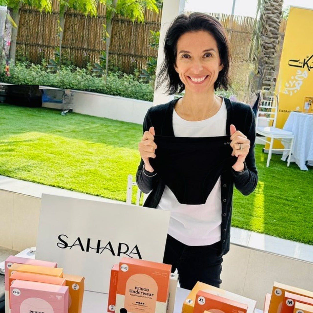Natalie Hobbs holding black period pants in front of a Sahara brand display outdoors.